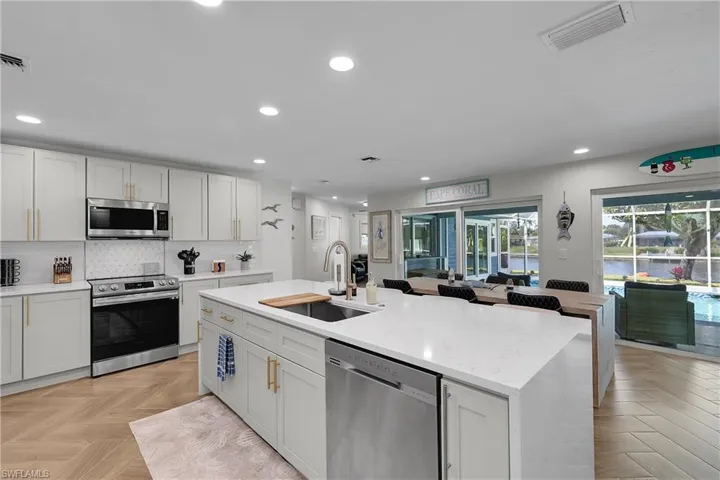Kitchen featuring a large island with sink, white shaker-style cabinetry, stainless steel appliances, and wood-finish flooring