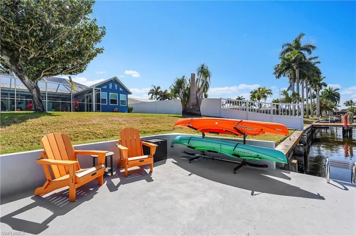 Waterfront patio with direct canal access, featuring a concrete surface, a permanent dock structure, and mature palm trees
