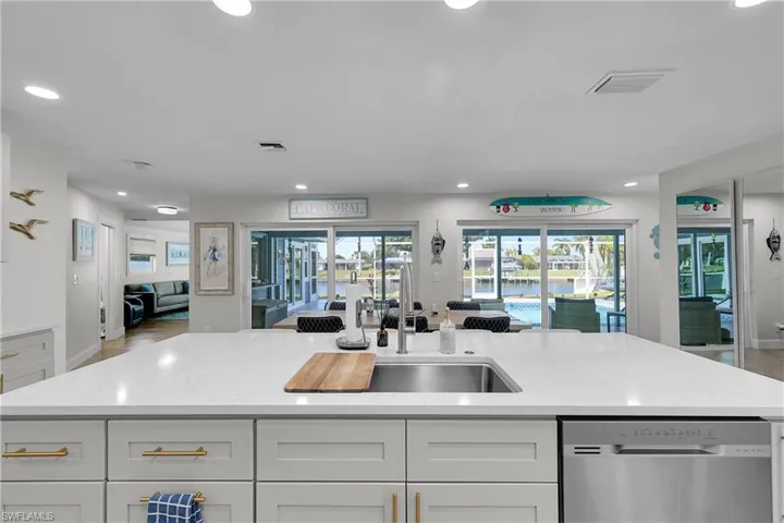 Spacious kitchen island featuring a stainless steel sink with an integrated cutting board, light-toned countertop, and white shaker-style cabinetry with gold-toned hardware
