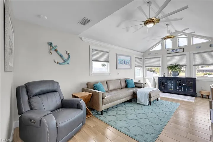 Vaulted ceiling sunroom featuring wood-finish flooring, multiple windows with blinds, and two large ceiling fans