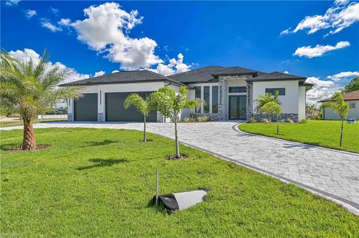 Prairie-style home with stone siding, a front yard, stucco siding, curved driveway, and an attached garage