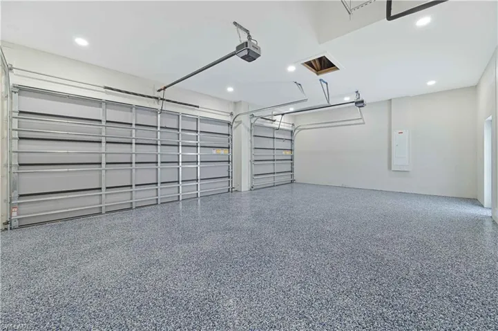 Garage with electric panel, recessed lighting, and a garage door opener
