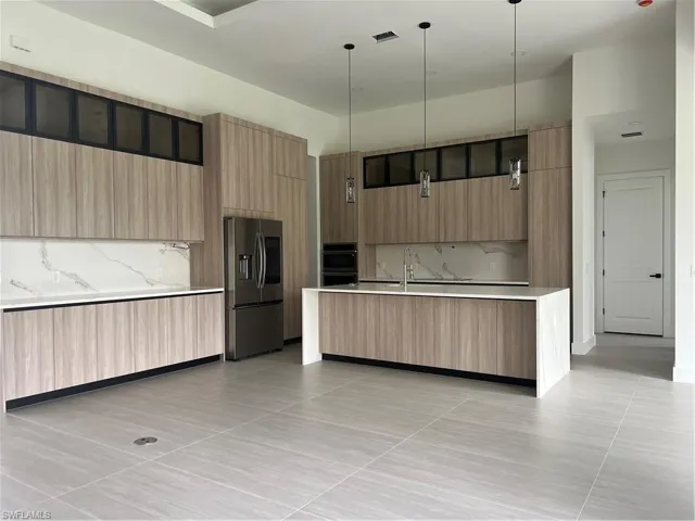 Kitchen featuring a kitchen island with sink, modern cabinets, decorative light fixtures, refrigerator, and decorative backsplash