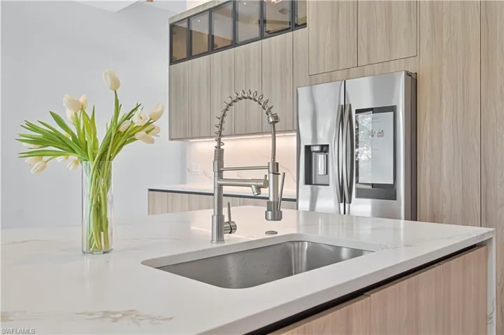 Kitchen featuring modern cabinets, stainless steel fridge with ice dispenser, light wood finish cabinets, light stone counters, and glass fronted cabinets