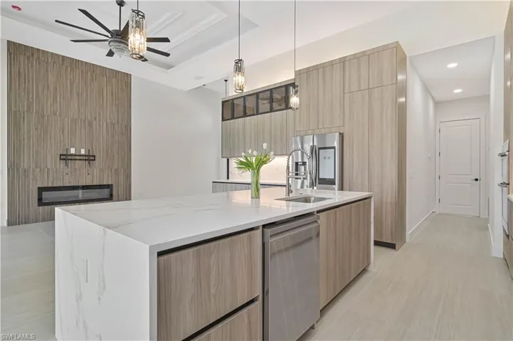 Kitchen featuring modern cabinets, light wood finish cabinetry, a kitchen island with sink, light stone countertops, and pendant lighting