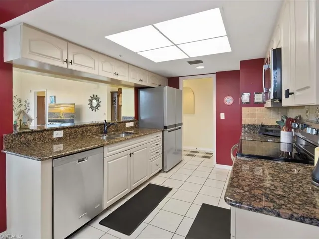 Kitchen with stainless steel appliances, dark stone counters, light tile patterned floors, and backsplash