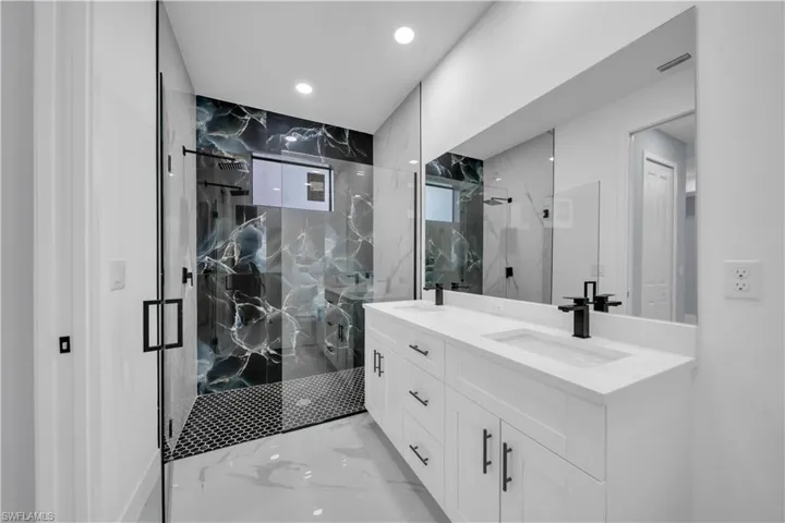 Bathroom with light marble finish floors, a marble finish shower, double vanity, and recessed lighting