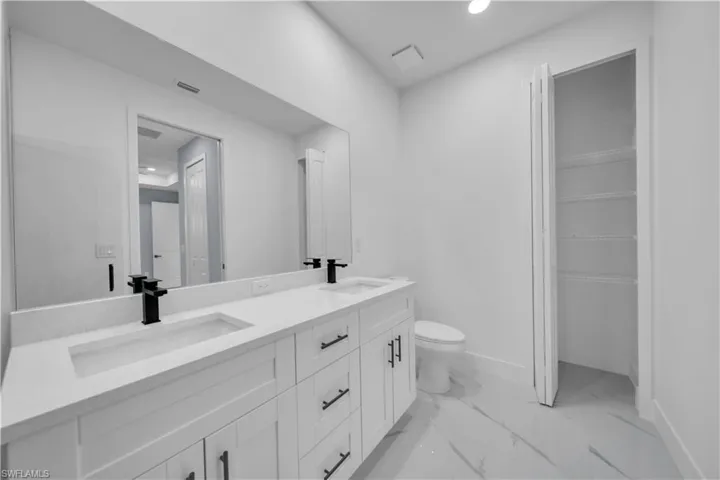 Bathroom with double vanity, light marble finish flooring, recessed lighting, and a walk in closet