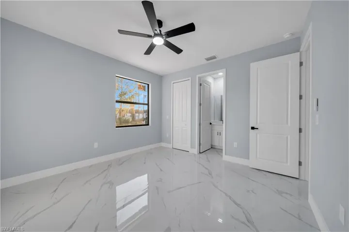Unfurnished bedroom with ceiling fan, light marble finish floors, a closet, and ensuite bath