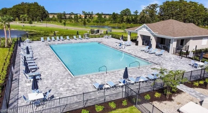 Community swimming pool with extensive paver decking, a dedicated pool house, and surrounding black metal fencing