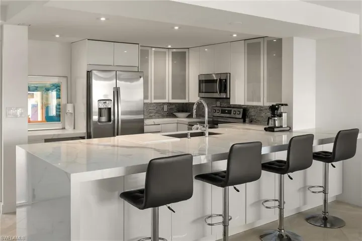 Kitchen featuring a peninsula, light stone counters, appliances with stainless steel finishes, a kitchen breakfast bar, and recessed lighting