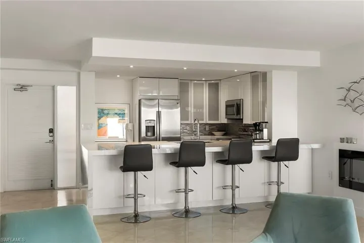 Kitchen featuring stainless steel appliances, backsplash, a kitchen bar, a peninsula, and white cabinetry