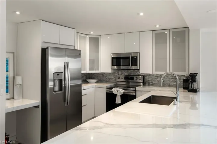 Kitchen with white cabinets, stainless steel appliances, modern cabinets, light stone countertops, and recessed lighting