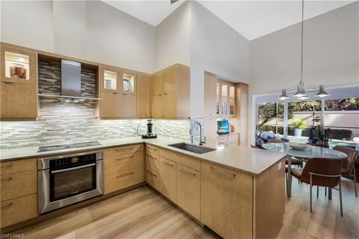 Kitchen featuring wood-finish cabinetry, stainless steel oven, cooktop, and range hood, mosaic tile backsplash, and light-toned countertops