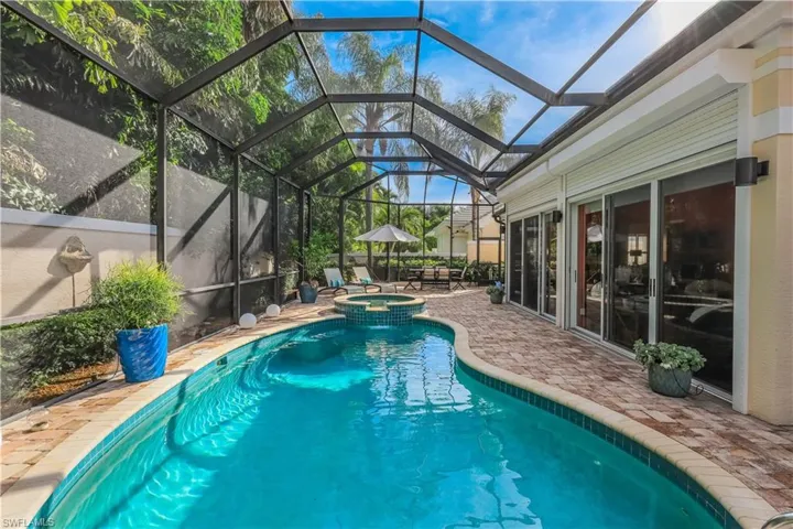 Screened pool enclosure featuring a curvilinear pool, integrated spa, and brick-patterned hardscaping