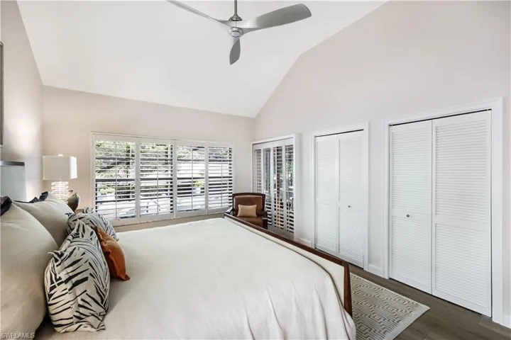 Vaulted ceiling with contemporary ceiling fan, expansive window with white plantation shutters, and wood-finish flooring