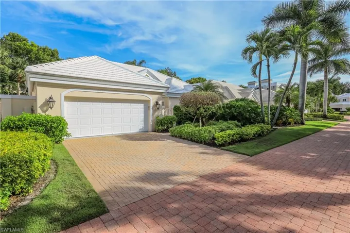 Exterior featuring a white paneled garage door, decorative sconces, a tiled roof, and lush landscaping