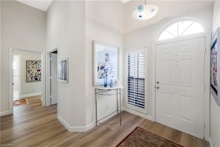 Vaulted ceiling entry foyer featuring wood-finish flooring, a white paneled entry door, and an arched transom window