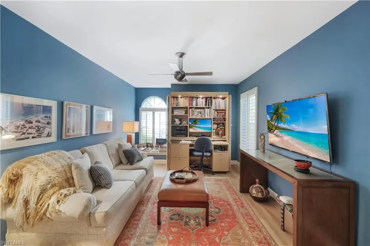 Wood-finish flooring, built-in desk and shelving unit, window with arched transom, and ceiling fan with integrated lighting