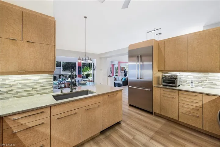 Kitchen featuring wood-finish cabinetry, stainless steel refrigerator, stone countertops, and tile backsplash