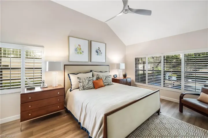 Vaulted ceiling, wood-finish flooring, white plantation shutters, and a modern ceiling fan