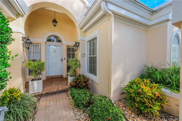 Arched entryway featuring a brick paver walkway, decorative exterior lighting, and a front door with an arched transom