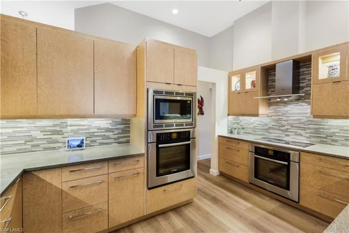 Modern kitchen featuring natural wood-finish cabinetry, stainless steel appliances, a linear tile backsplash, and light-toned countertops