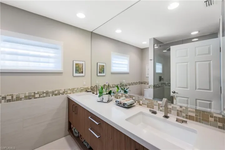 Dual sinks with brushed nickel fixtures, white countertop, wood-finish vanity with drawer storage, mosaic tile backsplash, and recessed lighting