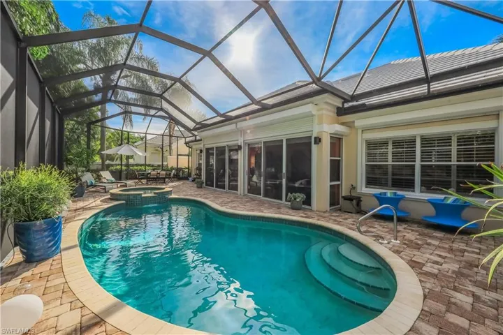 Screened-in outdoor living space featuring a freeform pool, integrated spa, and paver patio