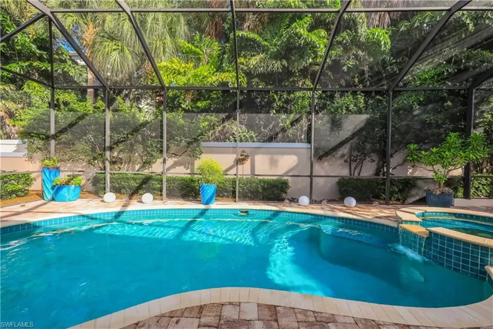 Screened enclosure featuring a freeform swimming pool, integrated spa with waterfall, and paver decking