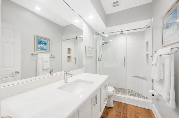 Bathroom featuring hardwood / wood-style flooring, vanity, toilet, and a shower with door