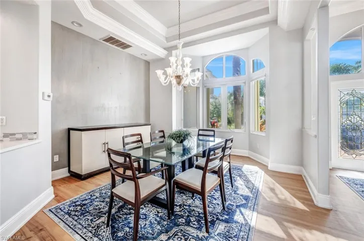 Dining room with light wood-type flooring, a raised ceiling, ornamental molding, and an inviting chandelier