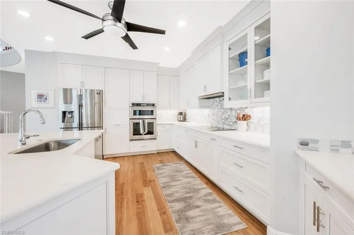 Kitchen with sink, backsplash, white cabinetry, appliances with stainless steel finishes, and light hardwood / wood-style floors