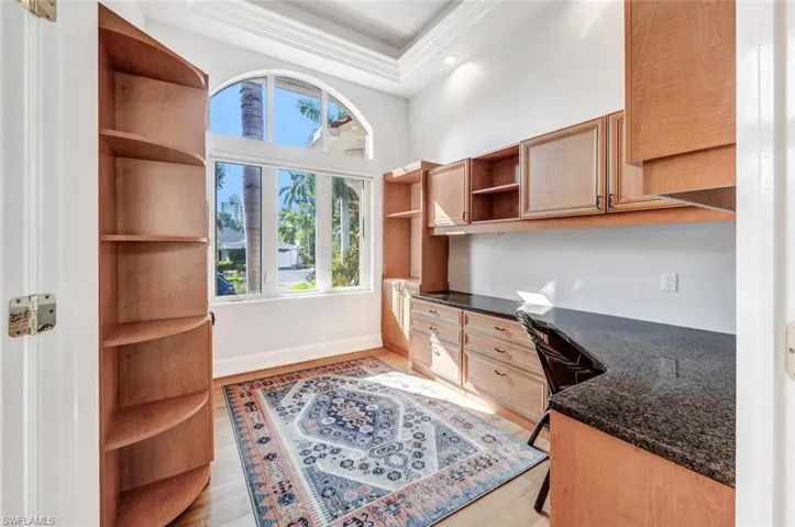 Office area with light hardwood / wood-style flooring, a wealth of natural light, built in desk, and a raised ceiling