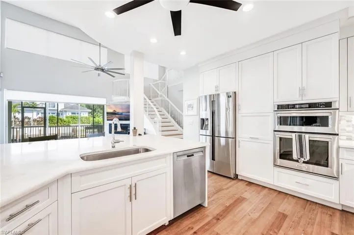 Kitchen featuring appliances with stainless steel finishes, white cabinetry, tasteful backsplash, light wood-type flooring, and sink