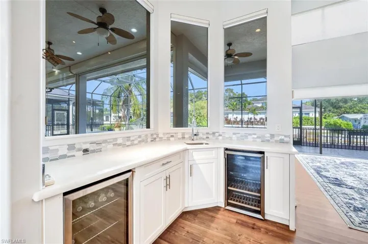 Bar featuring beverage cooler, light hardwood / wood-style flooring, and backsplash