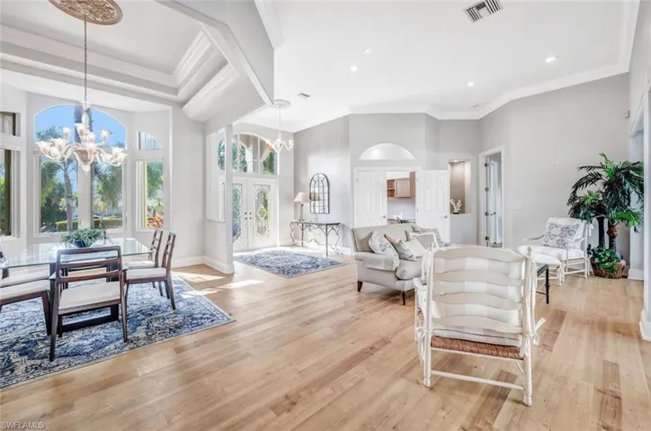Living room with a notable chandelier, light hardwood / wood-style flooring, a towering ceiling, crown molding, and french doors