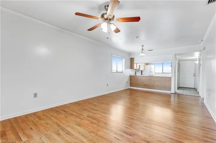 Unfurnished living room with light hardwood / wood-style flooring, ornamental molding, and ceiling fan