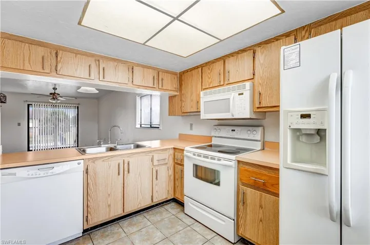 Kitchen with white appliances, light tile patterned flooring, sink, and a wealth of natural light