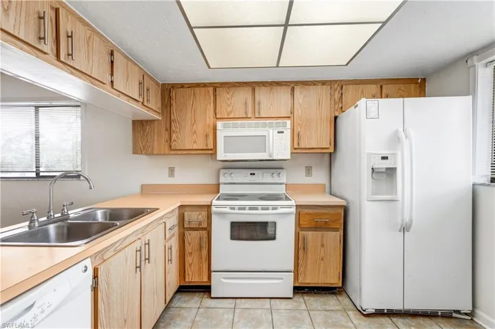 Kitchen featuring sink, light tile patterned flooring, and white appliances