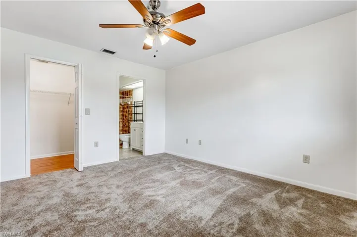 Unfurnished bedroom with a closet, a walk in closet, ensuite bath, light colored carpet, and ceiling fan