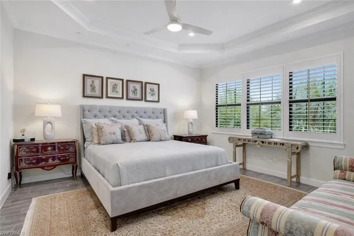 Primary Bedroom with porcelain wood-like flooring, ceiling fan, crown molding, tray ceiling, with recessed lighting and sweeping serene views of the lake and preserves
