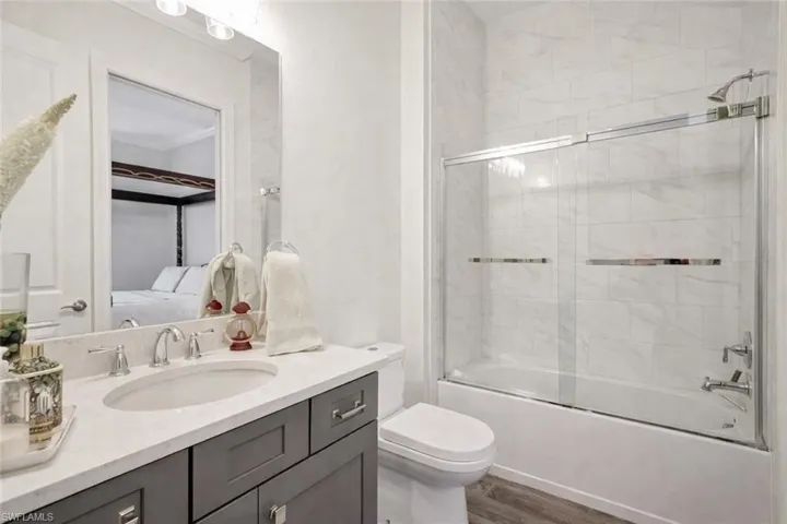 Recently painted walls, front guest full bath with enclosed glass shower / bath combination  vanity, porcelain wood-like tiled floors, and vanity