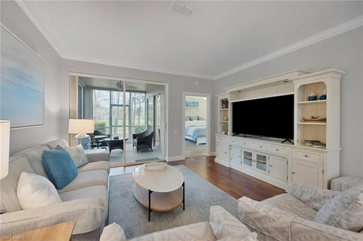 Living area with dark wood finished floors, ornamental molding, and a sunroom