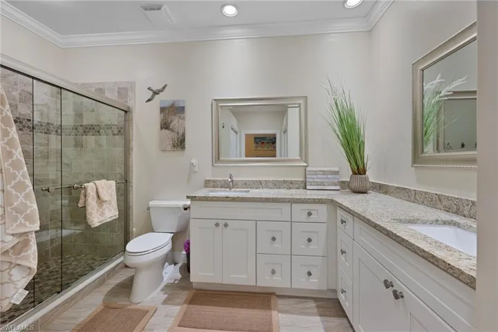 Full bathroom featuring double vanity, a shower stall, and crown molding