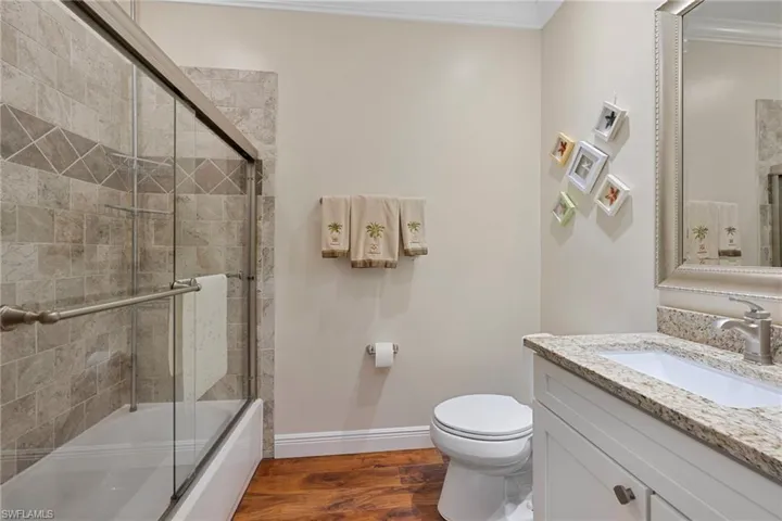 Bathroom featuring combined bath / shower with glass door, dark wood-style floors, vanity, and ornamental molding