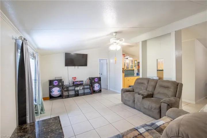 Living room with lofted ceiling, ceiling fan, and light tile floors