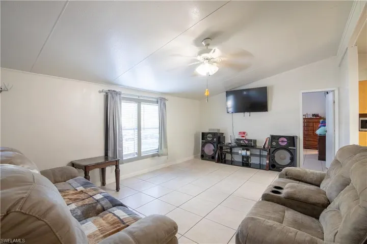 Tiled living room with ceiling fan, crown molding, and lofted ceiling