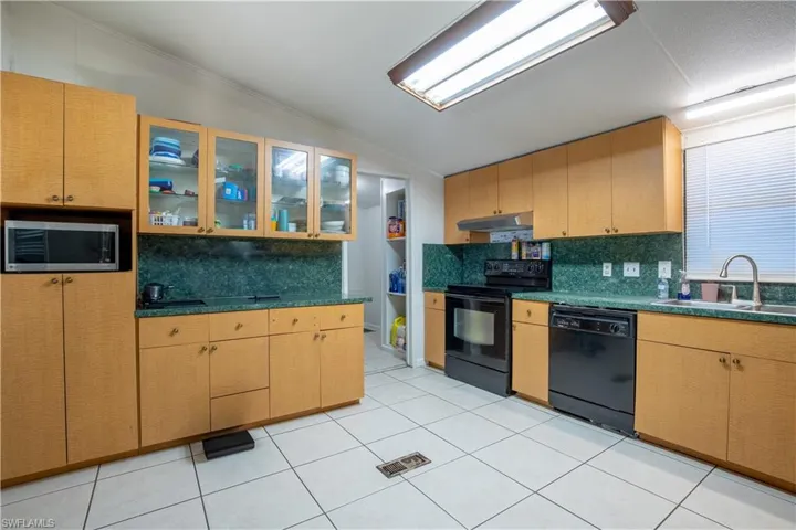 Kitchen with backsplash, black appliances, sink, light tile floors, and lofted ceiling