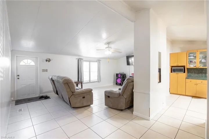 Living room with ceiling fan, vaulted ceiling, and light tile floors